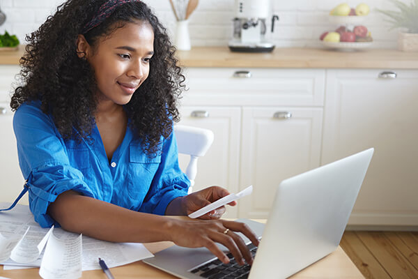 managing-and-budgeting-finances Woman tapping on a computer while holding a paper